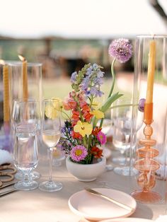 the table is set with flowers and wine glasses, candles, and plates on it