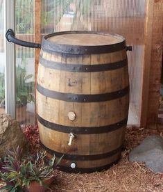 a wooden barrel sitting on top of dry grass next to rocks and plants in front of a window