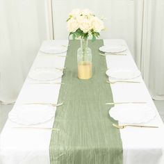 the table is set with white plates and green linens, along with a vase filled with flowers