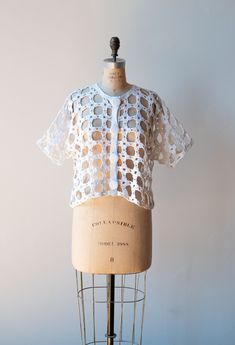 "Fun 1990s white crochet sweater by Michael Simon. Self fabric buttons at the front. Short sleeves. - Fits Up to size large - Bust: 44\" Waist: 45\" Length: 19\" Sleeve Length: 13\" Condition: Excellent! - Small mend at collar" White Knit Button-up Top, White Pointelle Knit Top For Daywear, White Pointelle Knit Cardigan For Daywear, Fitted White Knit Blouse, Spring Fitted Crochet Top With Buttons, Fitted Crochet Top With Buttons For Spring, White Fitted Crochet Top With Knit Fabrication, White Open Knit Blouse For Spring, White Crochet Top For Spring Daywear