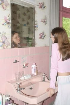 a woman standing in front of a bathroom sink with pink tiles on the wall behind her