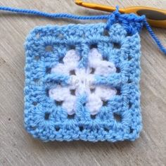 a crocheted square with two white flowers on it next to a pair of scissors