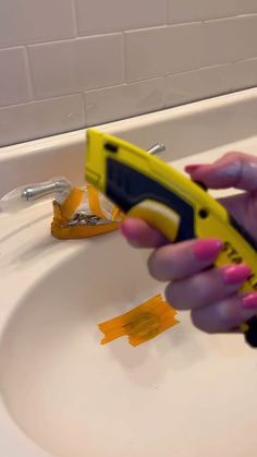 a woman holding a yellow and black device in front of a bathroom sink with orange tape on it