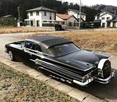 an old black car is parked on the side of the road