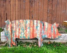 a wooden pig sculpture sitting on top of a green grass covered field next to a fence