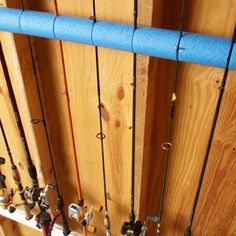 several fishing rods are lined up against a wooden wall with blue poles and hooks on it