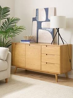 a living room with a white couch and wooden cabinet next to a potted plant