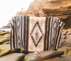 a woman standing on rocks holding up a blanket