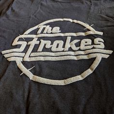 the strokes logo on a black t - shirt with white thread in front of it