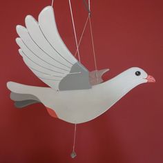 a white bird hanging from a string on a red wall in the shape of a dove