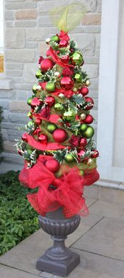 a small christmas tree with red and green ornaments on it's top, in front of a house