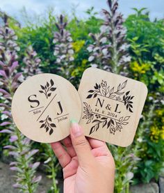 two wooden coasters with the initials and date printed on them, in front of purple flowers