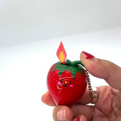 a hand holding a strawberry shaped keychain with a candle sticking out of it