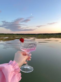 a person holding a wine glass with a cherry on it in front of a body of water