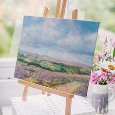 an easel with a painting on it next to flowers