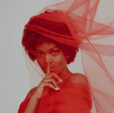 a woman in a red dress with a veil over her head and finger on her lips