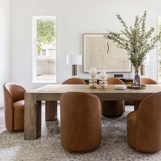 a dining room table surrounded by brown chairs and a vase filled with flowers on top of it