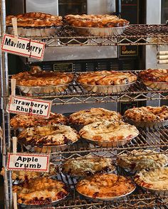 many pies are cooling in the oven on racks with signs that read marion berry, strawberry rhubart and apple crumb