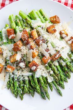 a white plate topped with asparagus covered in parmesan cheese and croutons