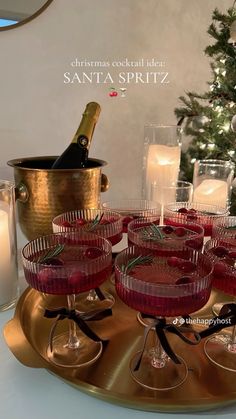 there are many glasses on the tray with wine and candles in front of the christmas tree