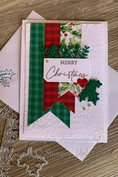 a christmas card with holly and mist on it, sitting next to two envelopes