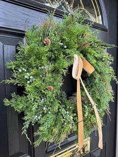 a wreath on the front door with pine cones and evergreens hanging from it's side