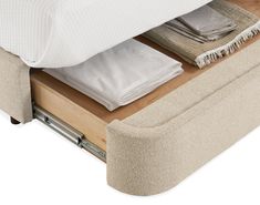 a bed with an open drawer underneath it that has folded sheets and blankets on top