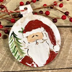 a christmas ornament with a santa clause painted on it and red berries in the background