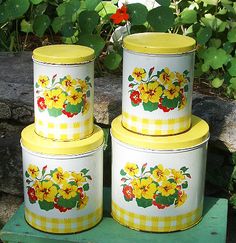 four yellow and white canisters with flowers painted on them sitting next to each other