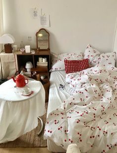 an unmade bed with white sheets and red polka dots on it, next to a small table