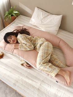 a woman laying on top of a pink pillow in a bed next to a potted plant