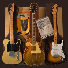 three guitars are lined up next to each other on a table with an old book