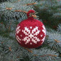 a red and white knitted ornament hanging from a pine tree