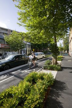 a man riding a bike down a street next to tall buildings and cars parked on the side of the road