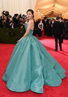 a woman in a blue gown standing on a red carpet with people behind her looking at the camera