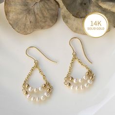 two pairs of earrings with pearls hanging from them on a white plate next to leaves