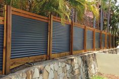 a stone wall with wooden slats along it and palm trees in the back ground