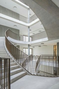 a spiral staircase in an empty building with concrete floors and white walls, leading up to the second floor