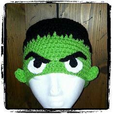 a green and black crocheted hat with eyes on top of a mannequin head