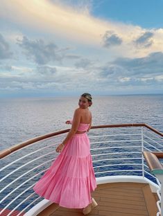 a woman in a pink dress standing on the deck of a cruise ship