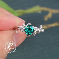 a close up of a person's hand holding a ring with a green stone