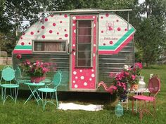 an old trailer is decorated with pink and green polka dots, while turquoise chairs sit in the grass