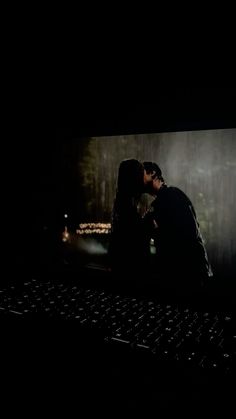 a man and woman kissing in front of a computer screen at night with the lights on