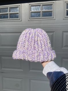 a hand holding up a knitted hat in front of a garage door