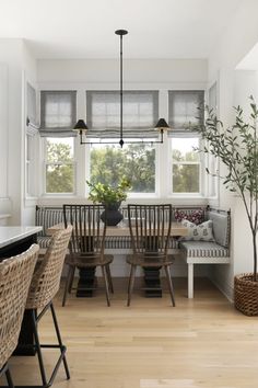 a dining room table with four chairs and a bench in front of the window, next to a potted plant