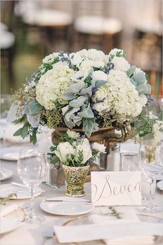 there is a vase with white flowers on the table and place cards in front of it