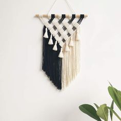 a black and white wall hanging with tassels next to a potted plant