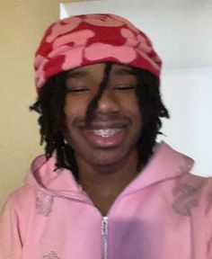 a man with dreadlocks and a pink hoodie smiles while holding a cell phone