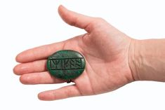 a person's hand holding a small green object with the word jesus on it