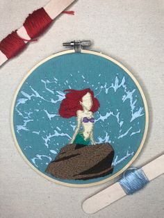 the little mermaid is sitting on top of a rock with her tail hanging down and she has red hair